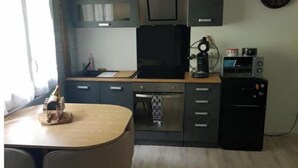 A compact kitchen with a dining table, a built-in oven, a coffee machine, and a small refrigerator.