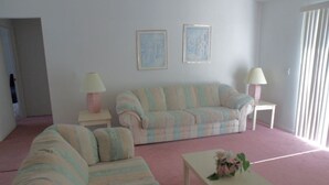Una sala de estar con un sofá a rayas, un sillón a juego, una mesita de centro pequeña y dos lámparas sobre mesitas auxiliares.