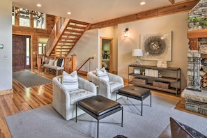 A spacious living area with a wooden staircase, a stone fireplace, and a cozy seating arrangement. - Luxe Cabin w/ Fireplace, Hot Tub, Game Room, Views (Banner Elk)