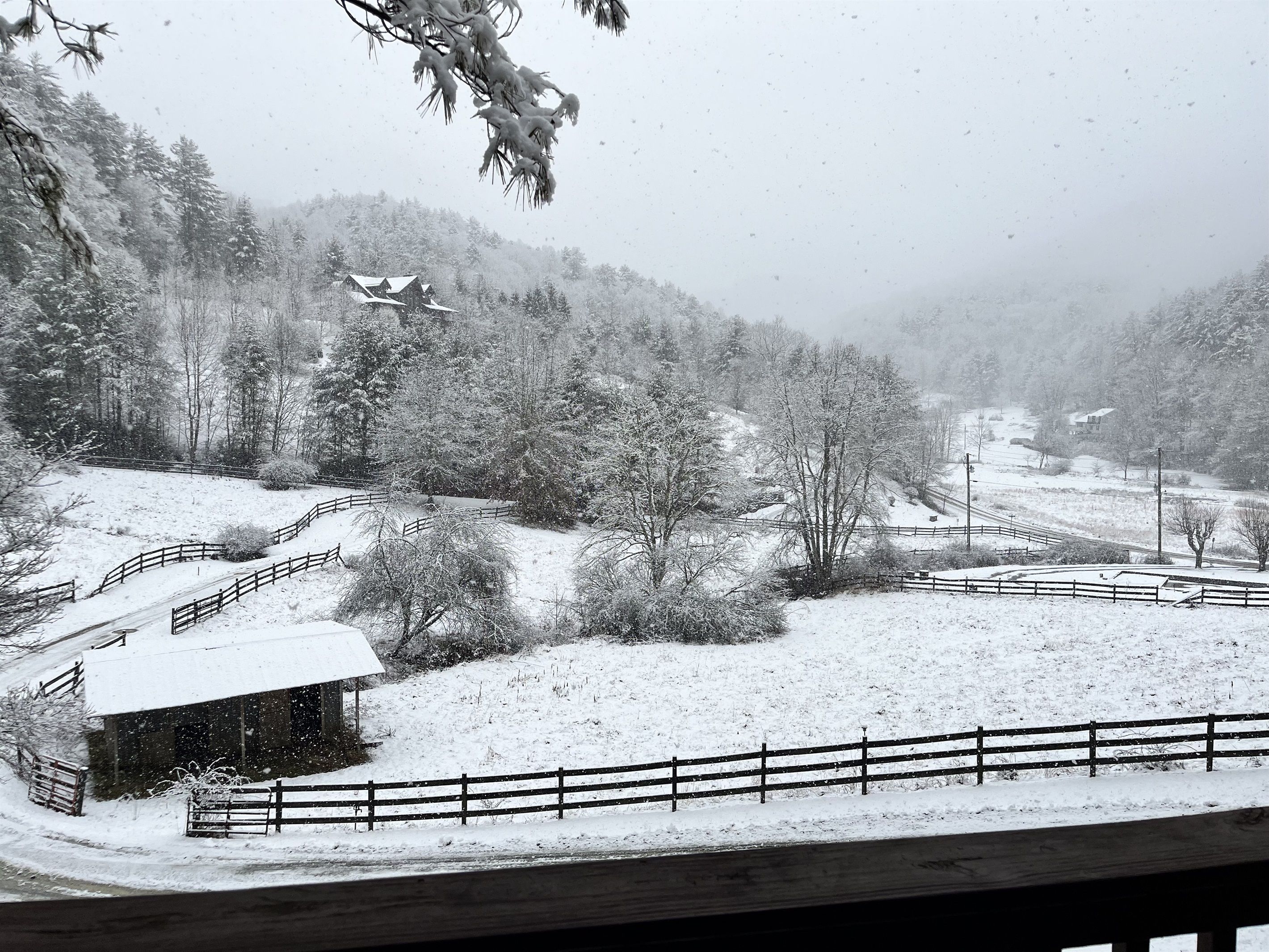 Ett snötäckt landskap med en timmerstuga, ett inhägnat område och en väg som slingrar sig genom landskapet.