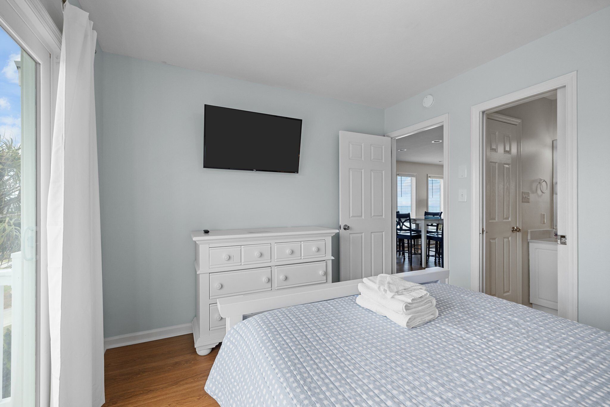 A bedroom with a bed, a dresser, a television, and a door leading to a balcony.