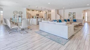 A spacious living area with a large white sofa, a dining table with chairs, and a kitchen in the background. - Huge, Popular Resort Villa 30+ Guests - Resort/Pool/Spa/Game Room/ Near Disney! (Davenport)