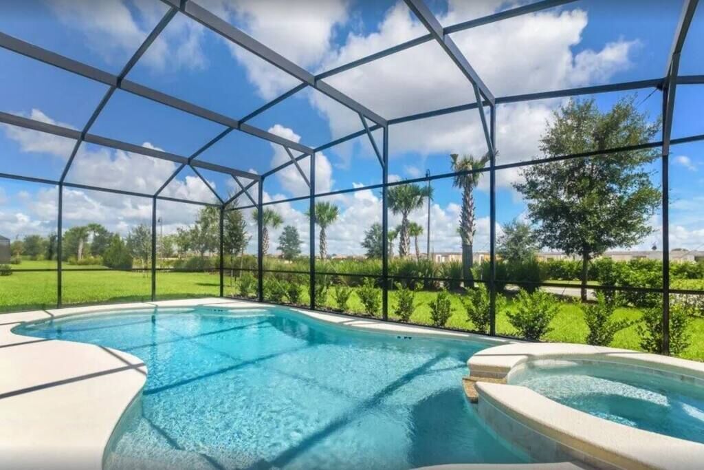 Ein Schwimmbad mit Glasveranda, umgeben von Grünpflanzen und blauem Himmel.