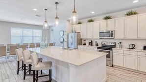 A modern kitchen with a large island, white cabinetry, stainless steel appliances, and pendant lighting. - Huge, Popular Resort Villa 30+ Guests - Resort/Pool/Spa/Game Room/ Near Disney! (Davenport)