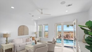 A spacious living room with a pool view, white walls, and a ceiling fan. - 🌅 16 Sunsets | Gulf Front | Private Pool | Free Sunset Dolphin Cruise | Beach Chair Service 🐬 (Miramar Beach)