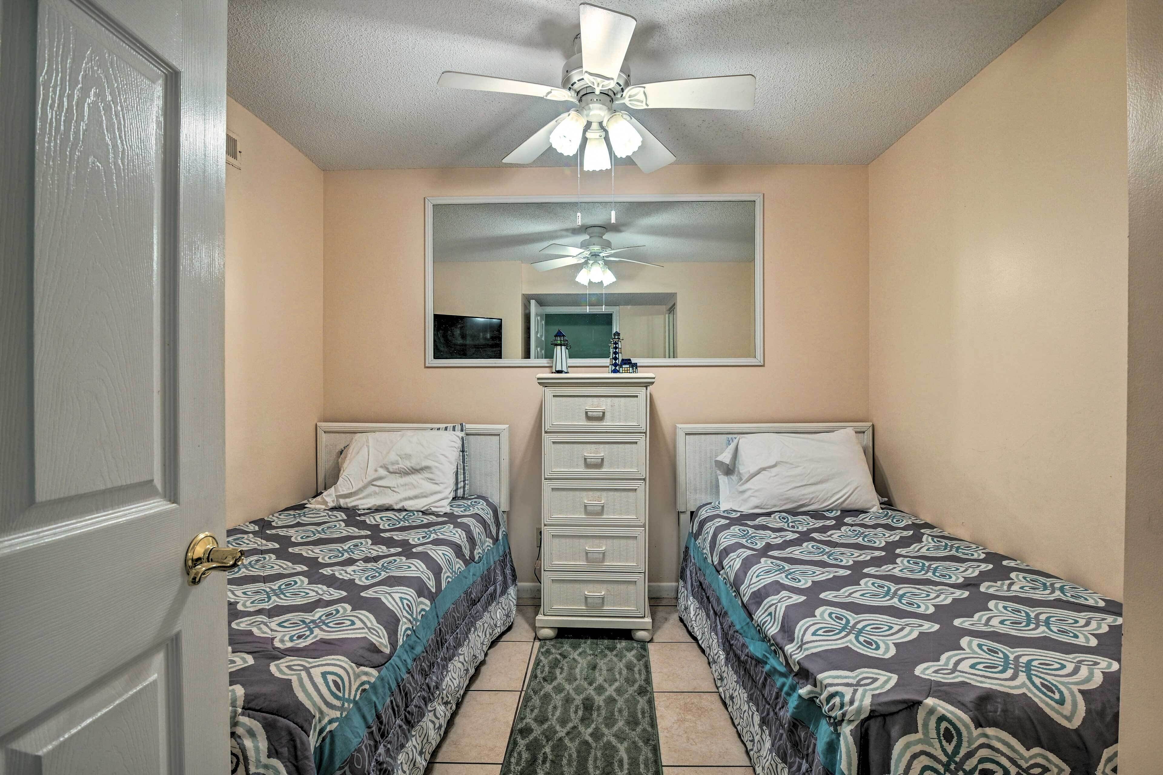 Un dormitorio con dos camas, un aparador, un ventilador de techo y un espejo grande.
