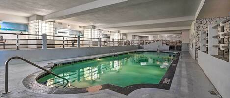 An indoor swimming pool with a concrete floor, a diving board, and a stone wall.