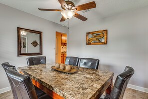 A dining room with a marble table, leather chairs, a ceiling fan, and artwork on the walls.