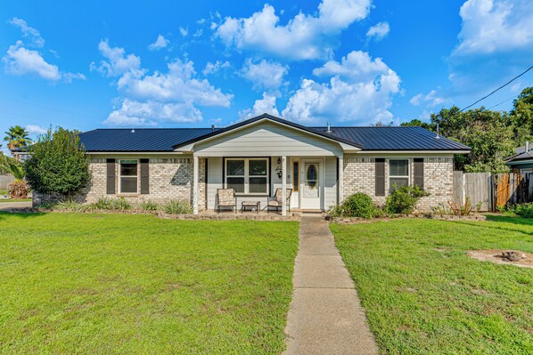 A single-story house with a front porch, a brick facade, and a metal roof.