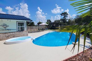 Une piscine avec un petit jacuzzi, un patio couvert et une maison avec un toit en métal.