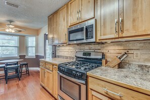 A kitchen with wooden cabinets, a gas stove, a microwave, and a dining area with a table and chairs.