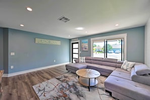 Una sala de estar moderna con un sofá modular, una mesa de centro redonda y una alfombra. Un letrero en la pared dice "BEACH HOUSE".