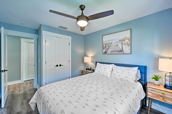 A bedroom with a bed, a ceiling fan, a nightstand with a lamp, a door, and a wall-mounted picture. - Walk to Beach: Getaway w/ Pool in Naples! (Naples)