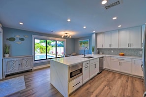 Una cocina moderna con armarios blancos, una isla grande y vistas a una piscina.