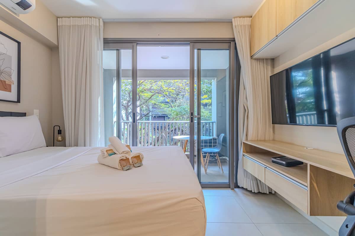 Habitación de hotel con cama, televisión, balcón con mesa y sillas, y puerta corrediza de vidrio.