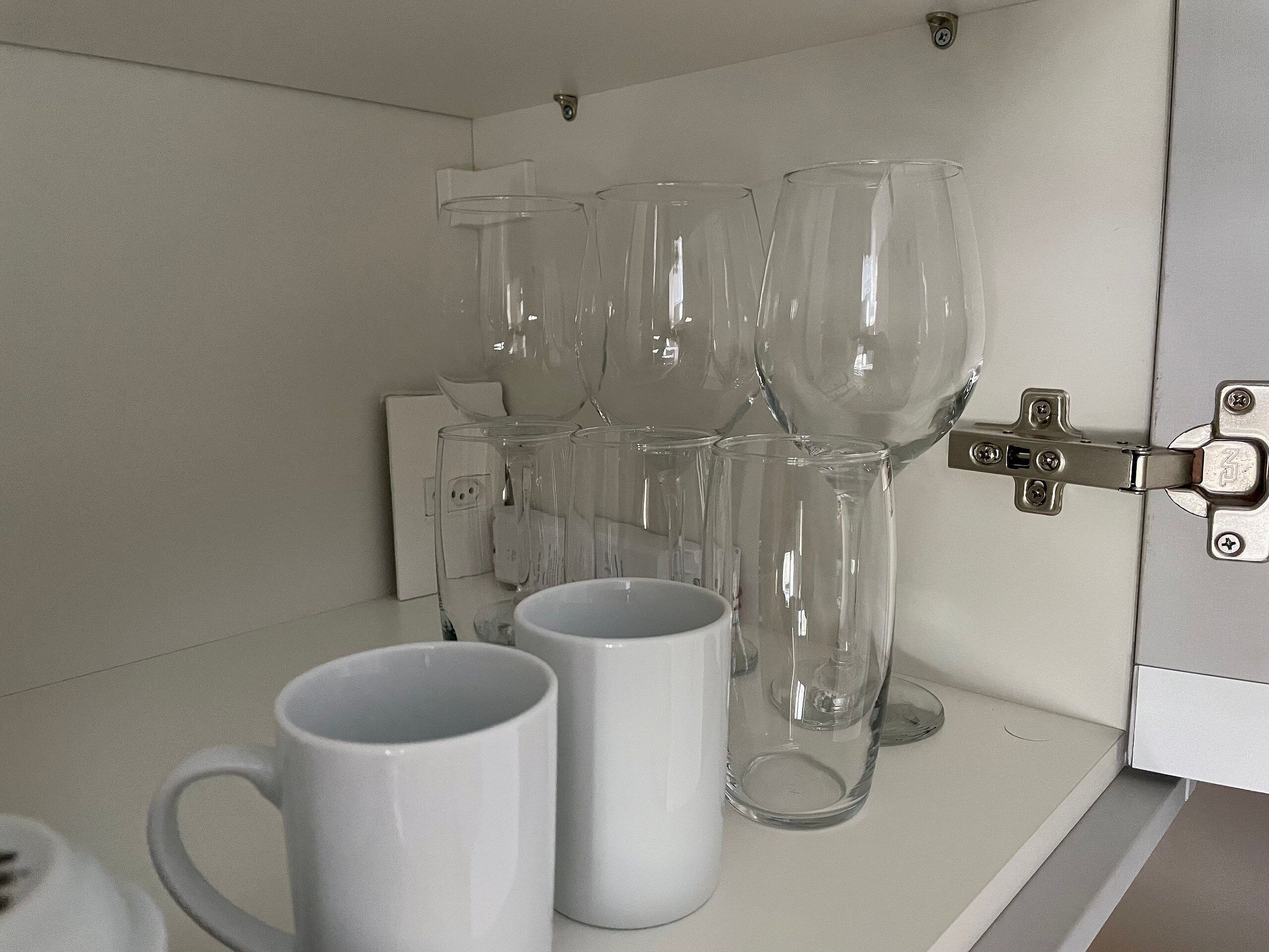 A kitchen counter with several clear glass mugs and a white cabinet with a metal latch.