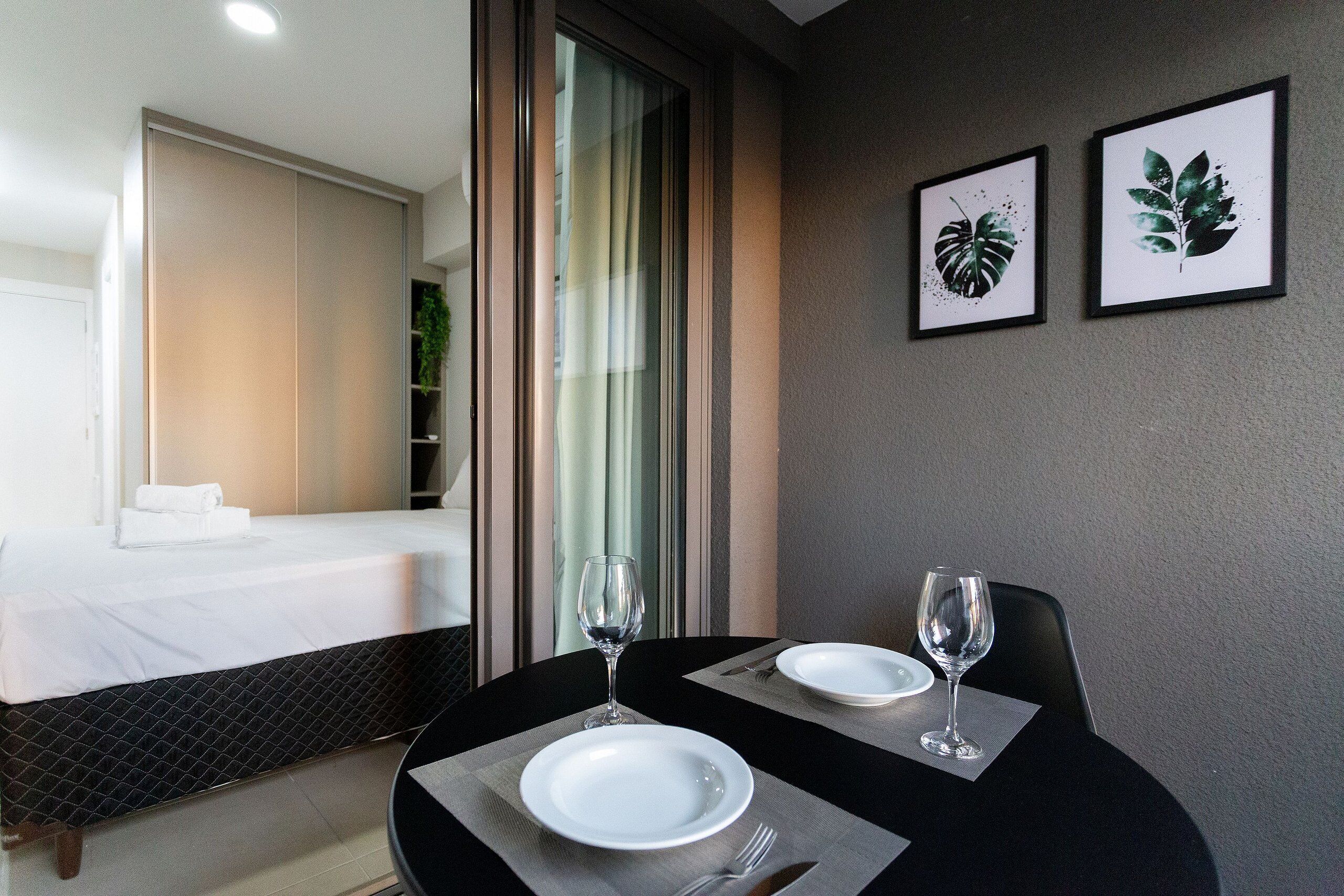 A hotel room with a bed, a dining table with plates and wine glasses, and two framed plant pictures on the wall.