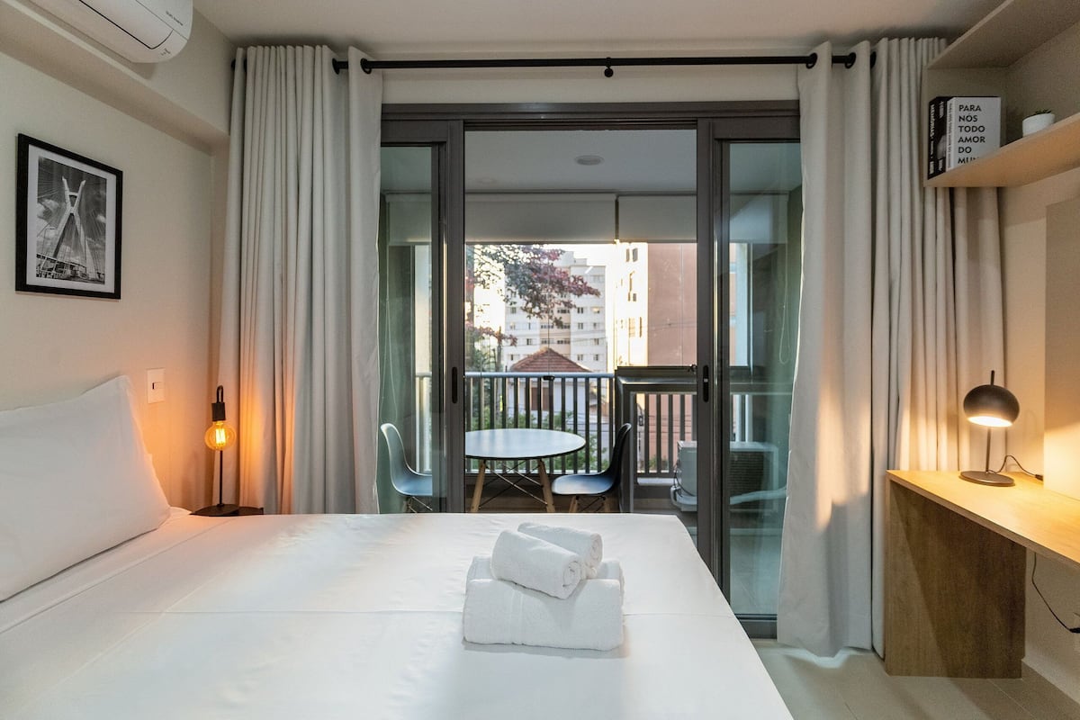 Habitación de hotel con cama, escritorio, silla y balcón con mesa y sillas.
