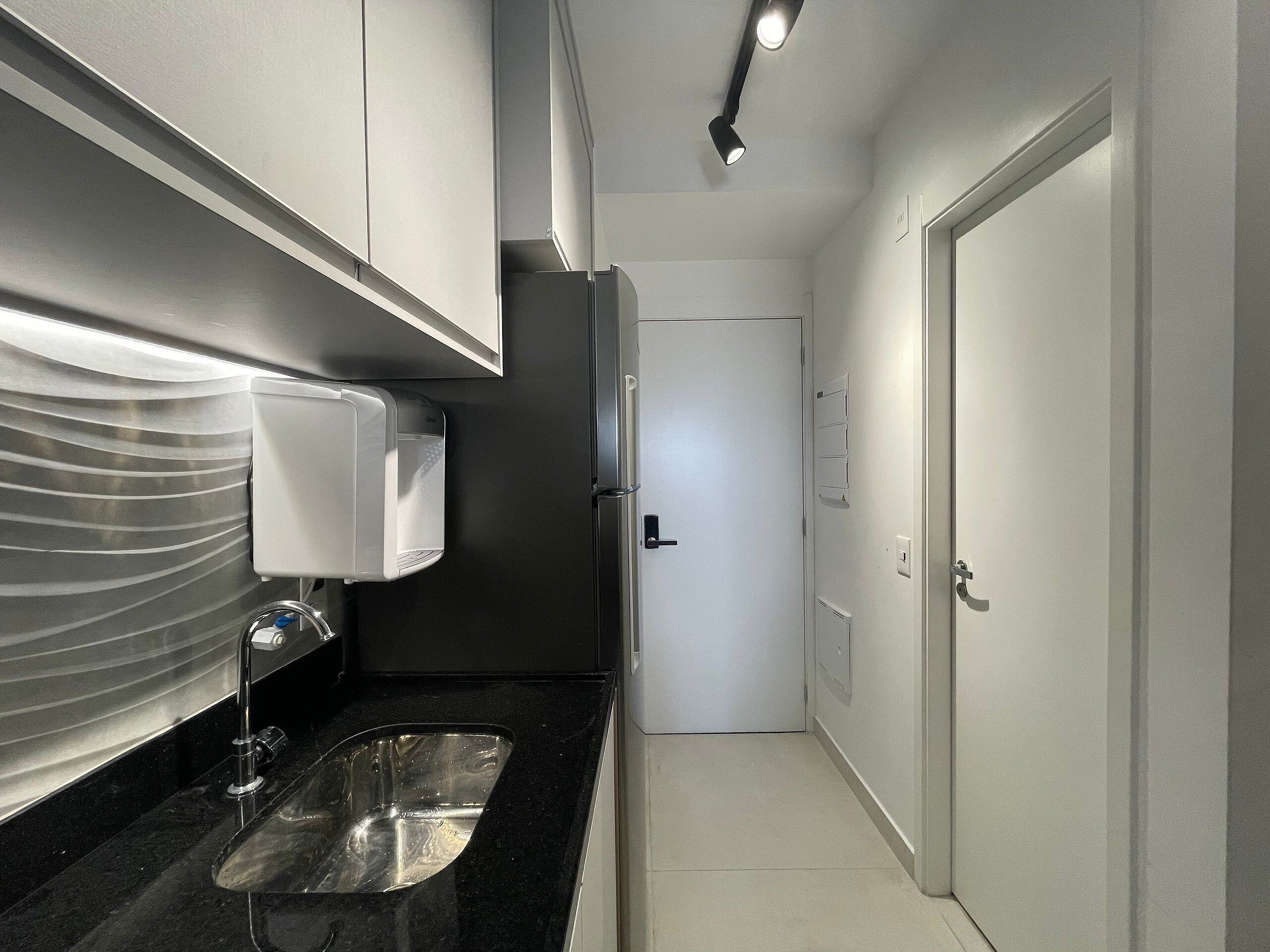 Una cucina angusta con un lavello in acciaio inossidabile, una porta bianca e un piano di lavoro nero.