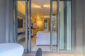 Une chambre d’hôtel moderne dotée d’une porte-fenêtre coulissante donnant sur un balcon, d’un lit, d’une petite kitchenette et d’un téléviseur à écran plat.