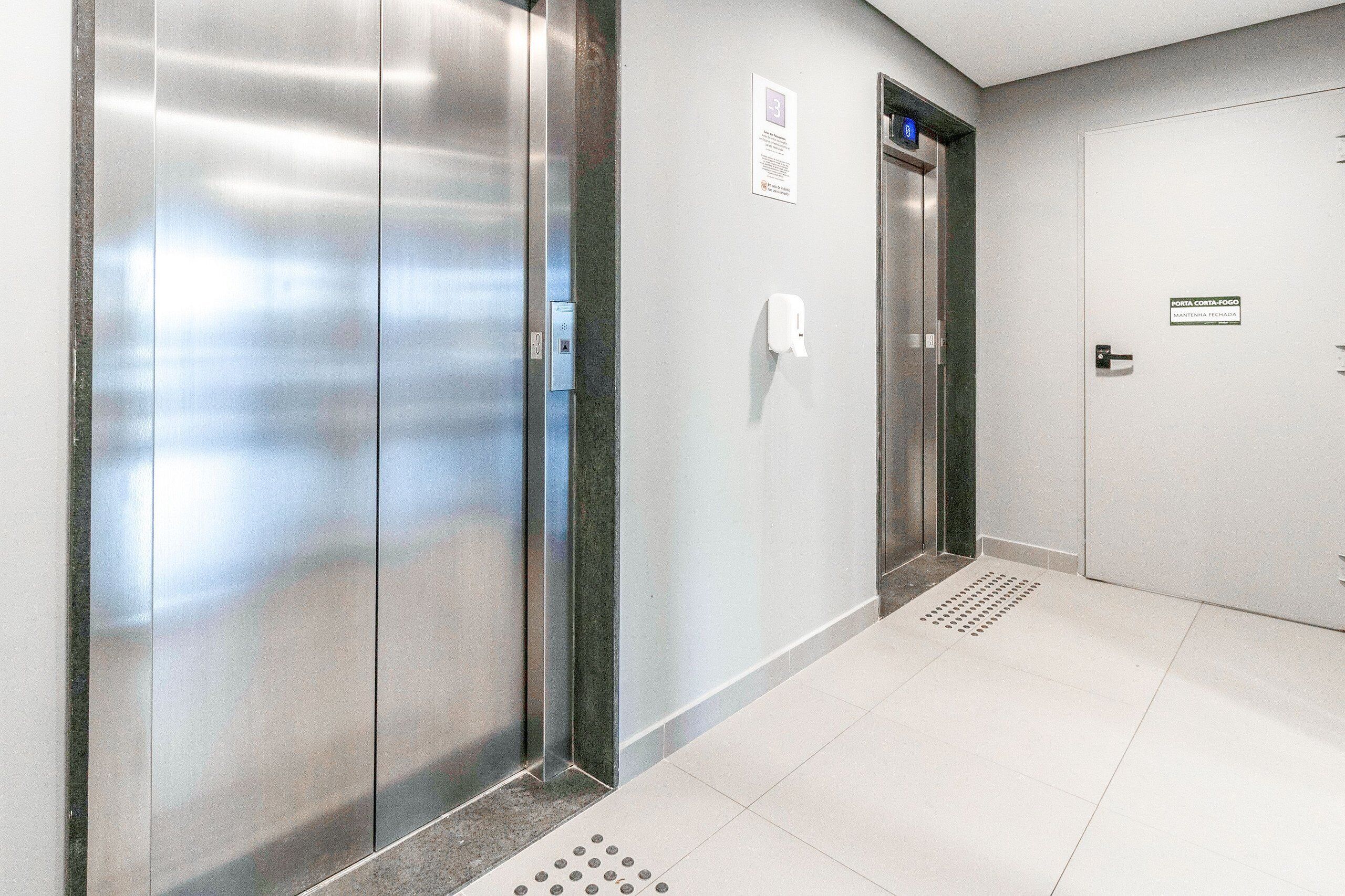 A modern elevator with a digital display, a wall-mounted hand sanitizer dispenser, and a door with a sign indicating the location.
