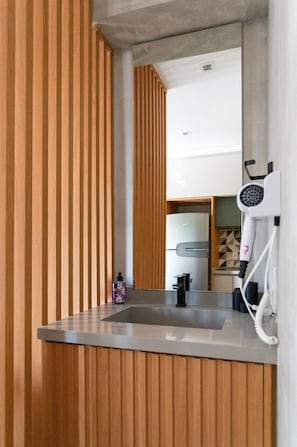 Ein modernes Badezimmer mit einer Wandpaneele aus Holz, einem großen Spiegel, einem Waschbecken und einem an der Wand befestigten Föhn.