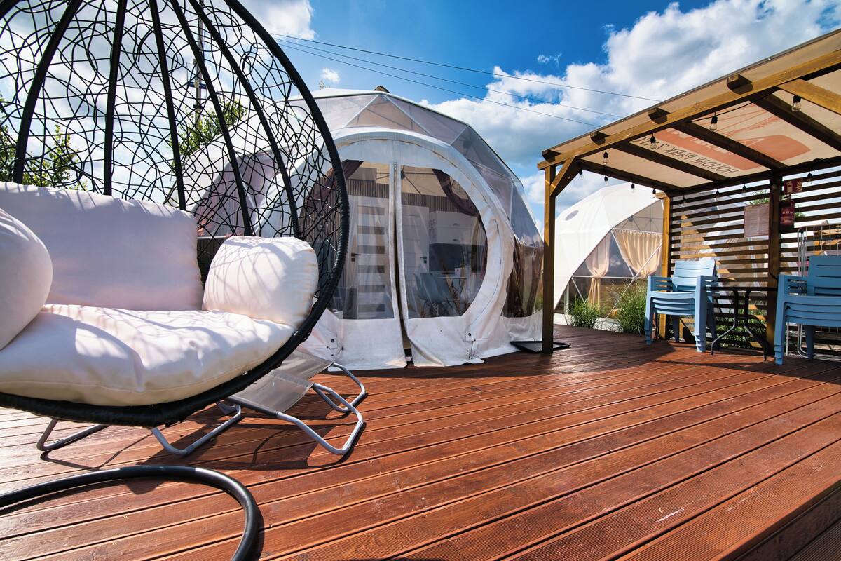 Une terrasse en bois avec un fauteuil suspendu et un espace abrité comprenant des tables et des chaises.