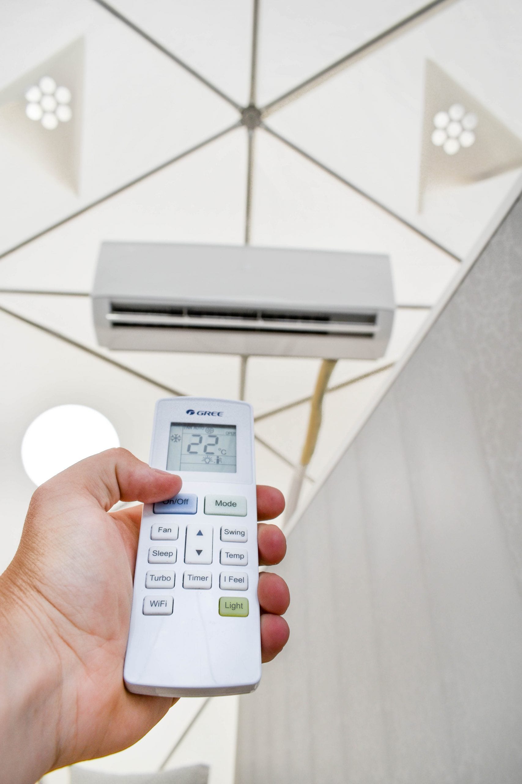 Eine Hand hält eine GREE Klimaanlagenfernbedienung, deren Digitalanzeige 22 Grad Celsius zeigt.