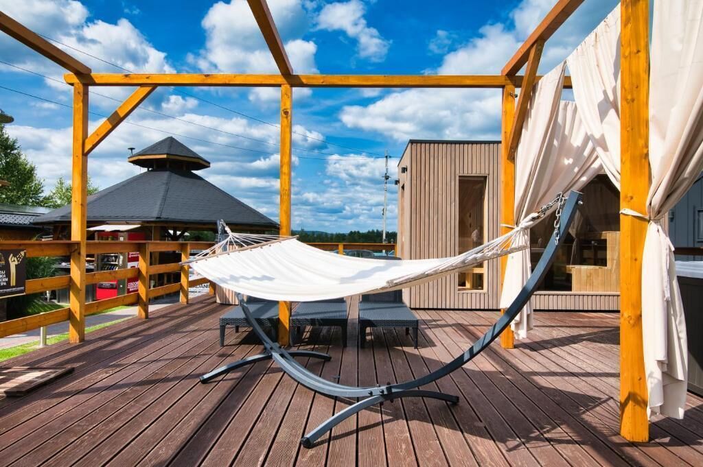 A wooden deck with a hammock, a covered seating area, and a building with a sloped roof.