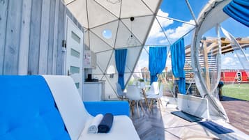 A tented accommodation with a blue sofa, white chairs, and a dining table.