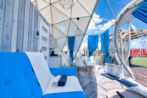 Un hébergement sous tente comprenant un canapé bleu, des chaises blanches et une table à manger.