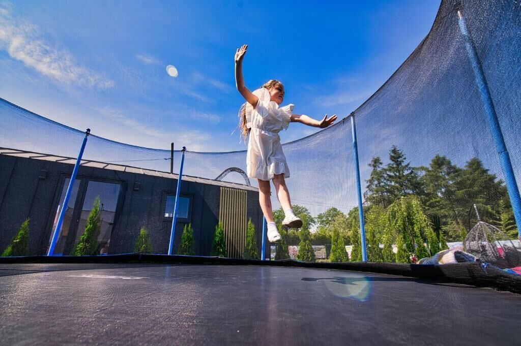 Un trampolín con barreras de seguridad de red, cielo despejado y árboles al fondo.