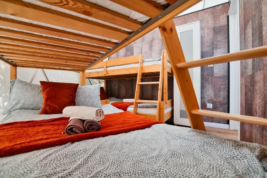 Habitación con literas, techo de madera, una ventana y una colcha roja en la cama.