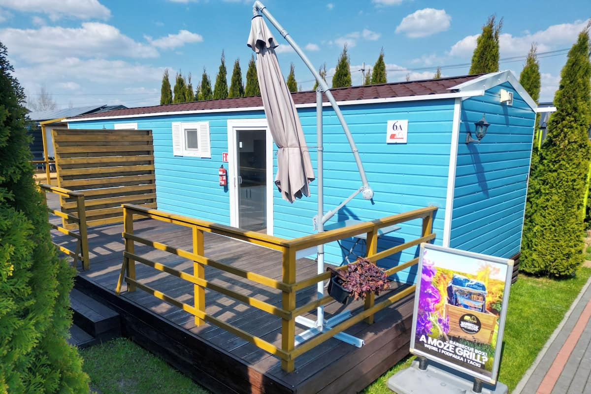 Un petit bâtiment d’un seul étage, à la façade bleue, doté d’une terrasse en bois et d’une enseigne annonçant un événement barbecue.