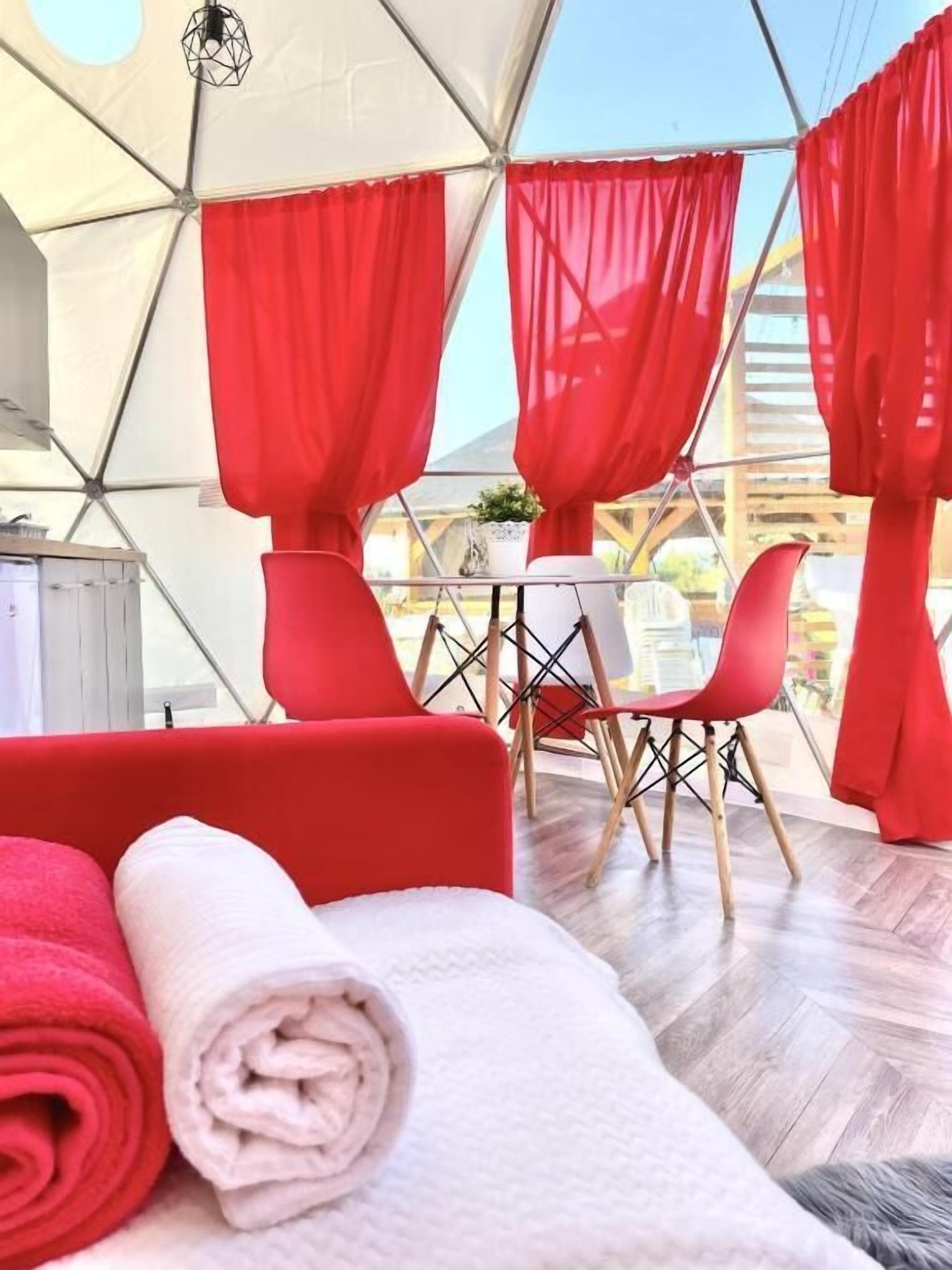 Quarto moderno com teto geométrico, cortinas vermelhas, um sofá vermelho e uma pequena mesa com cadeiras.