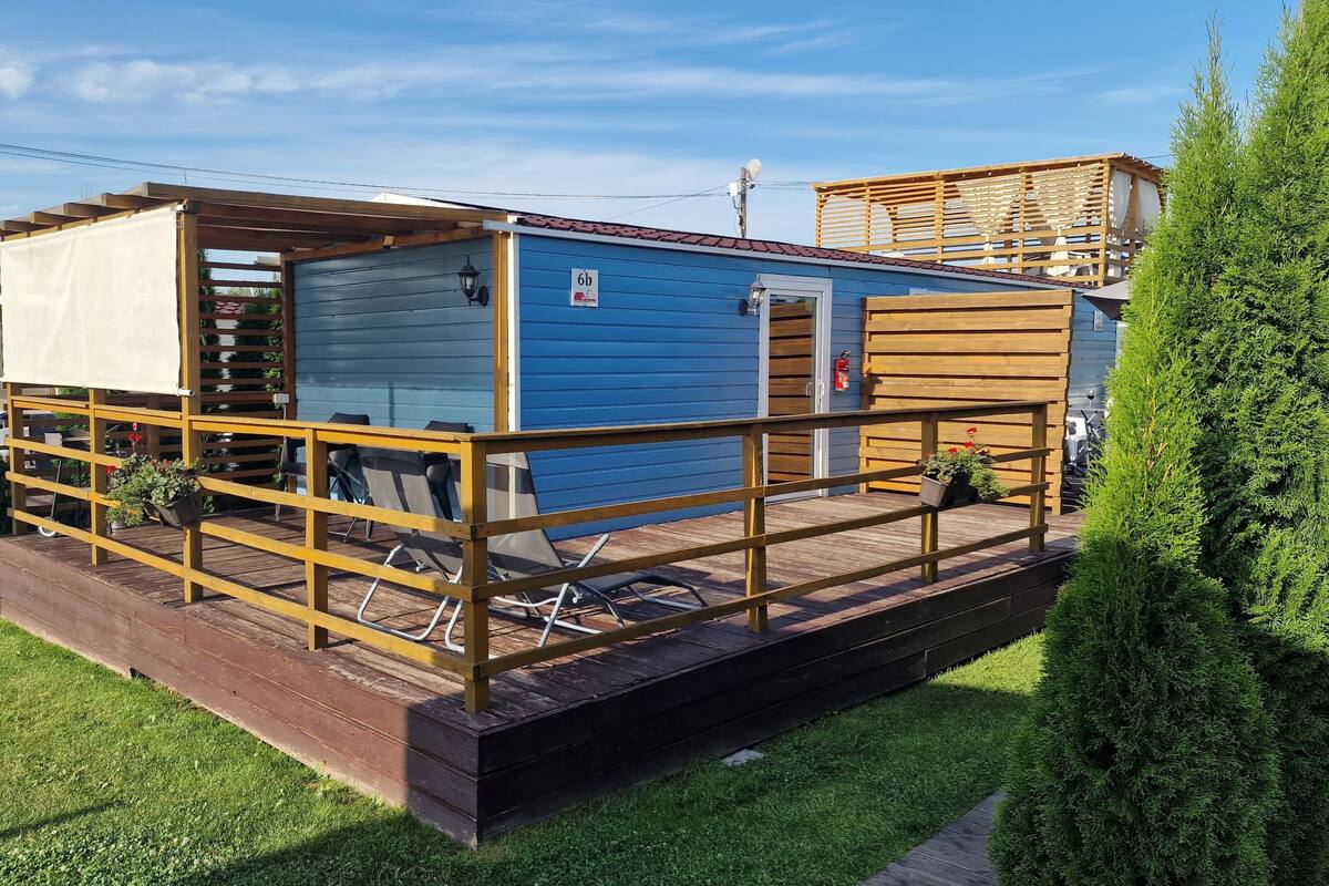 Une petite cabane bleue avec une terrasse en bois, un espace abrité et une porte portant le numéro 6D.