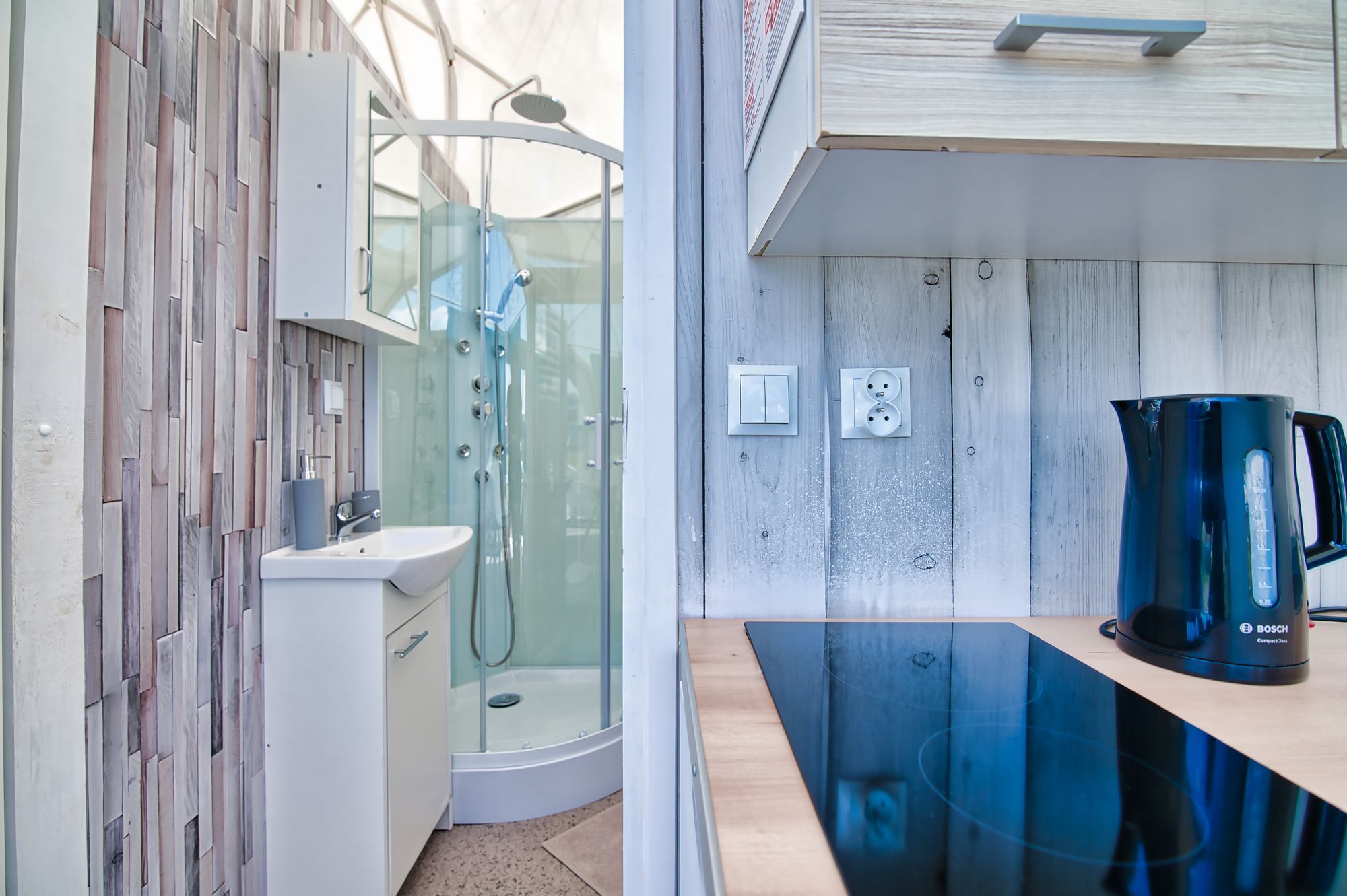 Ein modernes Badezimmer mit einer gläsernen Duschkabine, einem Waschbecken und einer Kaffeemaschine auf einer Holzauskleidung.