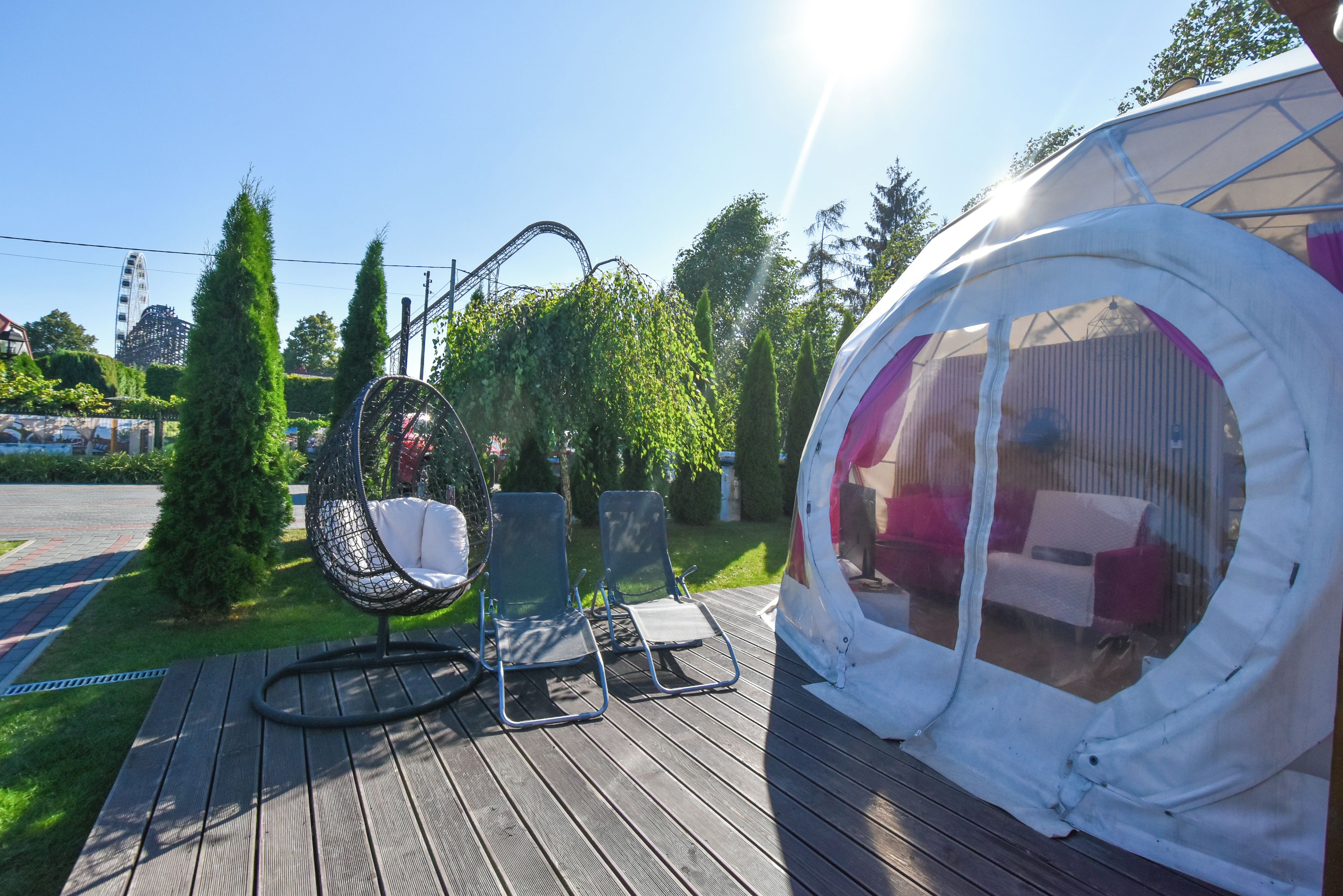 A wooden deck with a hanging chair, a circular tent-like structure, and a view of a roller coaster in the background.
