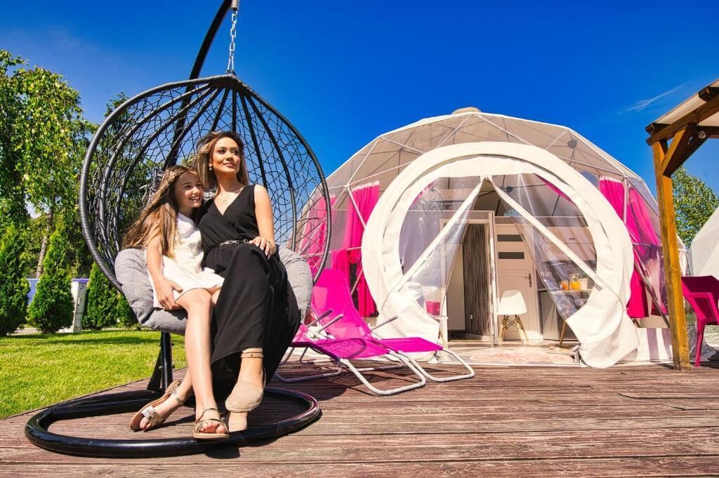 A wooden deck with a hanging chair and a dome tent.
