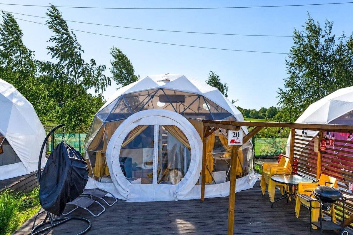 Une structure en forme de dôme géodésique dotée d’une fenêtre circulaire, d’une terrasse en bois et de mobilier d’extérieur.
