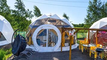 A geodesic dome structure with a circular window, a wooden deck, and outdoor furniture.