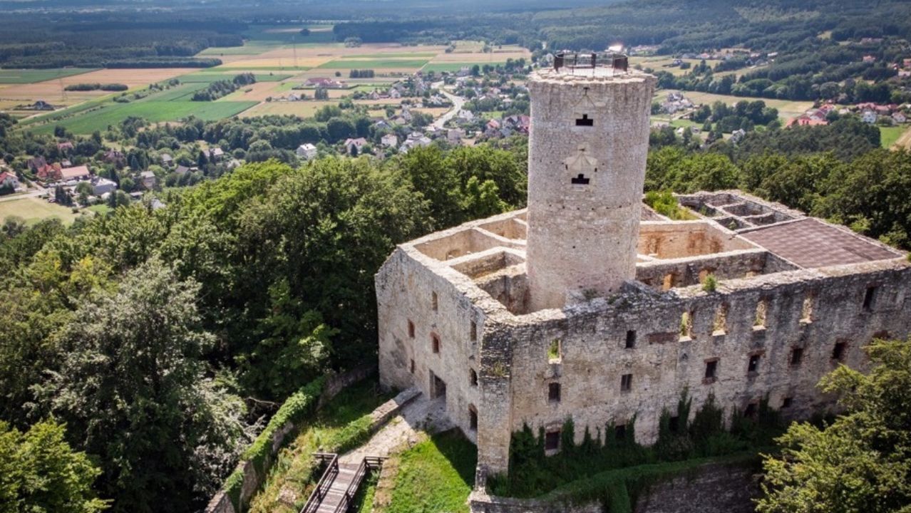 A historical stone castle with a central tower, surrounded by lush greenery and a rural landscape.