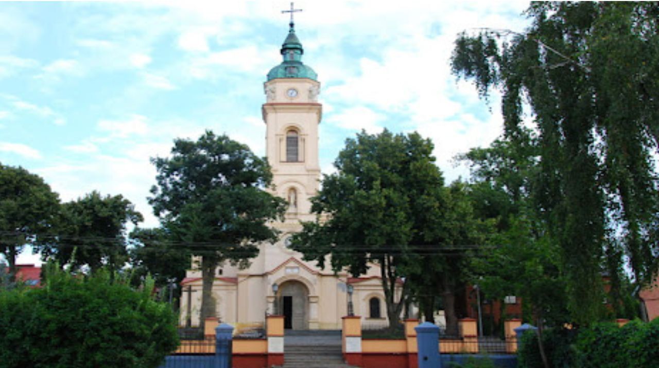 Uma igreja com uma alta torre do sino, cercada por árvores e um portão.