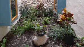 Un pequeño patio con pared de piedra, plantas en macetas y una jardinera central.