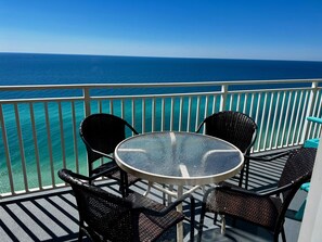 Un balcon avec une table ronde en verre et quatre chaises en osier, donnant sur une mer turquoise.
