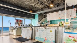 A café with a menu board, a Coca-Cola fridge, and a view of the beach.