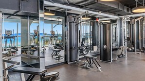 A gym with various exercise equipment, large windows offering a view of the beach, and a modern industrial design.