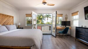 Une chambre avec un lit, un bureau, une chaise, une télévision et un balcon donnant sur des palmiers.
