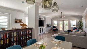 Un coin repas avec une table dressée pour quatre personnes, une bibliothèque et un salon avec un canapé et un téléviseur.