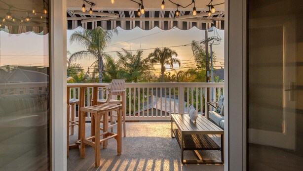Un balcon doté de mobilier en bois, de guirlandes lumineuses et offrant une vue sur des palmiers et le coucher de soleil.